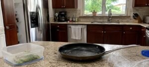 Cocina doméstica realista con sartén antiadherente, recipiente de plástico y papel film sobre encimera de granito