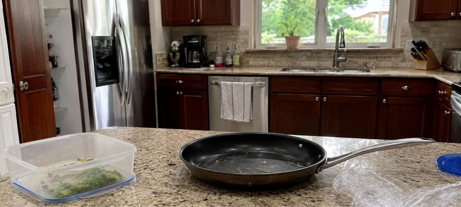 Cocina doméstica realista con sartén antiadherente, recipiente de plástico y papel film sobre encimera de granito